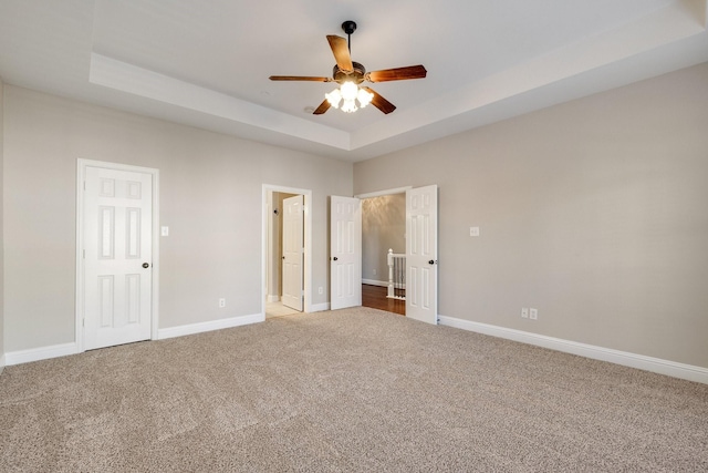 unfurnished bedroom featuring carpet floors, a tray ceiling, a ceiling fan, and baseboards