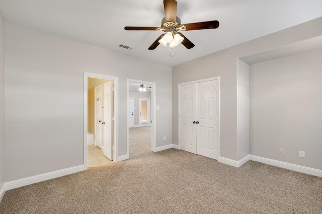 unfurnished bedroom with a closet, light colored carpet, ensuite bath, and ceiling fan