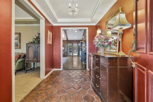 foyer with dark carpet, a raised ceiling, ornamental molding, and an inviting chandelier