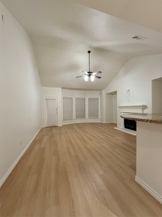 unfurnished living room with a textured ceiling, vaulted ceiling, light hardwood / wood-style floors, and ceiling fan