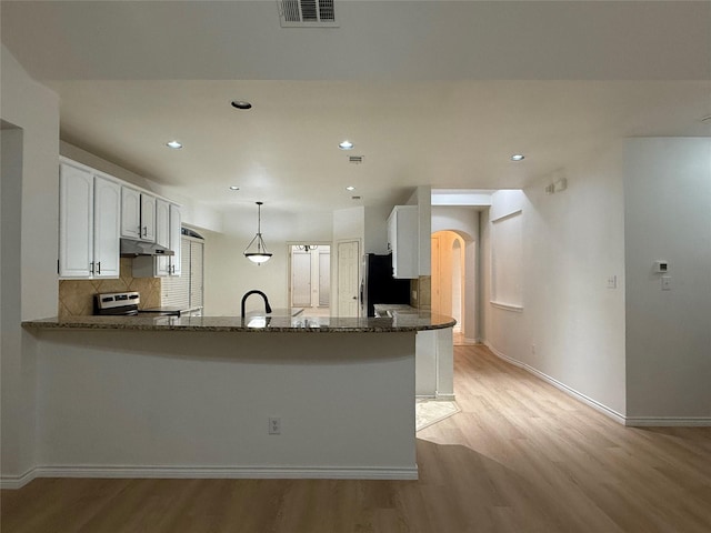 kitchen with appliances with stainless steel finishes, white cabinets, dark stone counters, hanging light fixtures, and kitchen peninsula