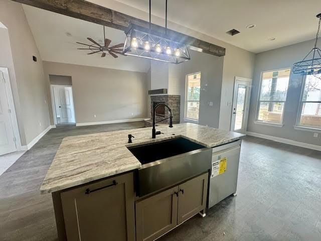 kitchen with light stone countertops, dishwasher, sink, decorative light fixtures, and a kitchen island with sink