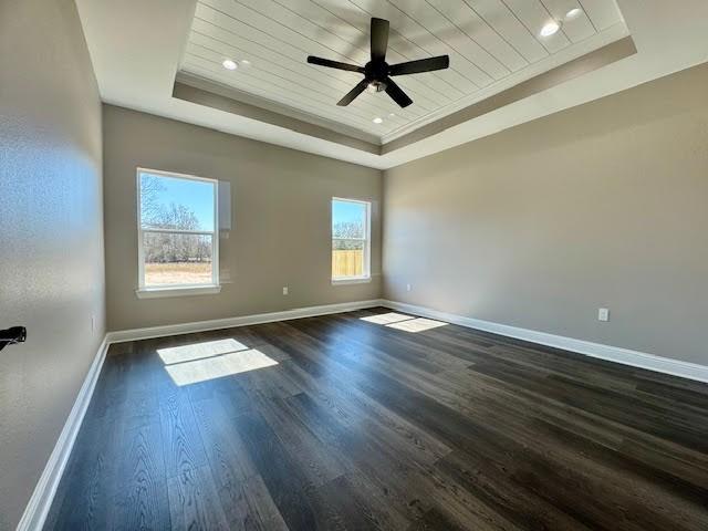 empty room with a tray ceiling, dark hardwood / wood-style flooring, and wooden ceiling