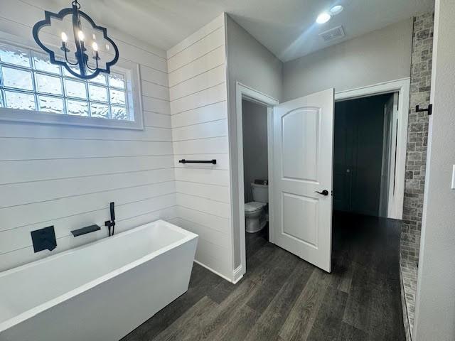 bathroom featuring hardwood / wood-style floors, toilet, a bathing tub, and a notable chandelier