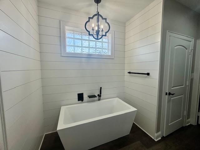 bathroom with a bath, an inviting chandelier, and wooden walls