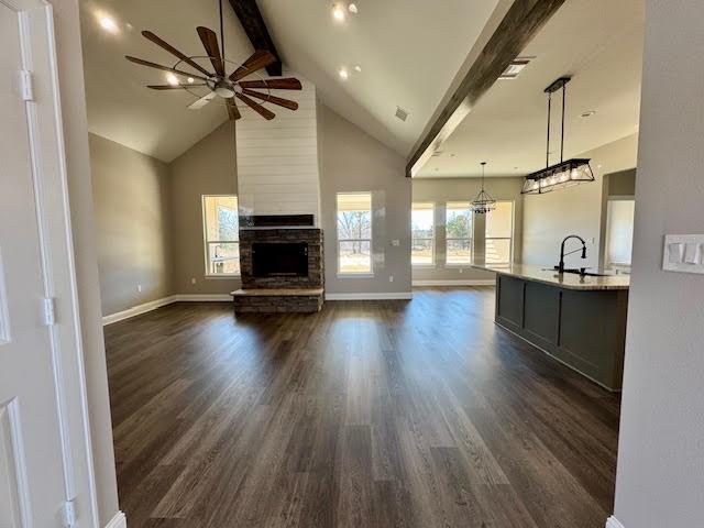 unfurnished living room featuring beamed ceiling, a stone fireplace, dark wood-type flooring, and sink