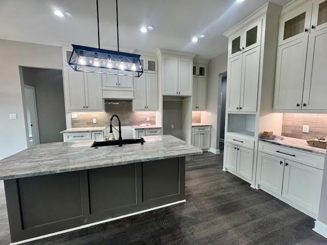 kitchen featuring white cabinets, sink, hanging light fixtures, and an island with sink