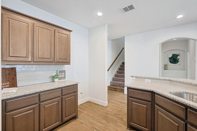 kitchen with sink, light stone countertops, light wood-type flooring, and backsplash