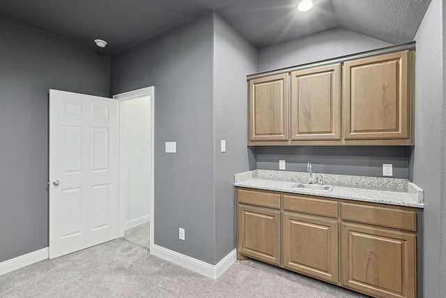 kitchen with baseboards, brown cabinets, a sink, and light colored carpet