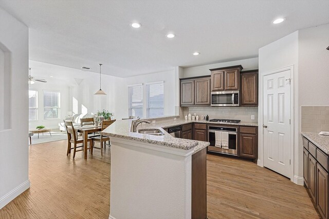 kitchen with kitchen peninsula, light wood-type flooring, stainless steel appliances, and sink