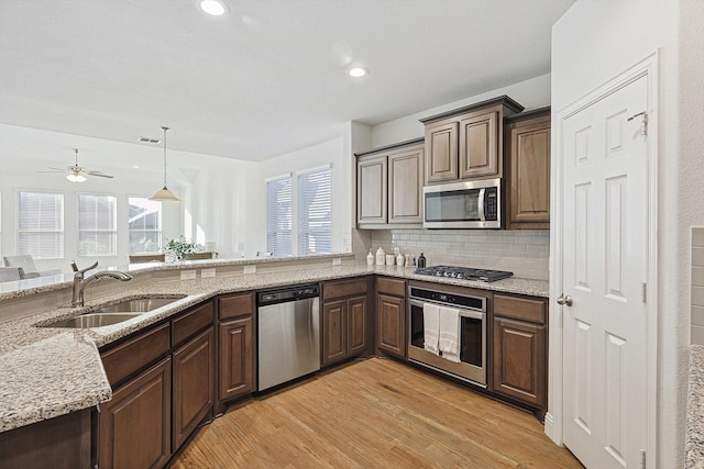 kitchen featuring stainless steel appliances, backsplash, light wood-style floors, a sink, and light stone countertops