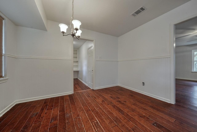 unfurnished dining area featuring dark hardwood / wood-style floors, wood walls, and a chandelier