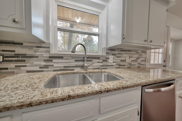 kitchen featuring tasteful backsplash, light stone counters, stainless steel dishwasher, sink, and white cabinets