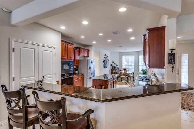 kitchen featuring a breakfast bar, black appliances, dark stone countertops, light tile patterned floors, and kitchen peninsula