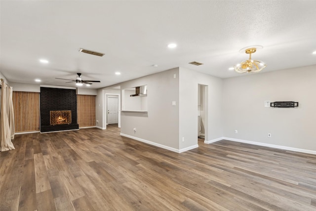 unfurnished living room with a fireplace, wood-type flooring, and ceiling fan with notable chandelier