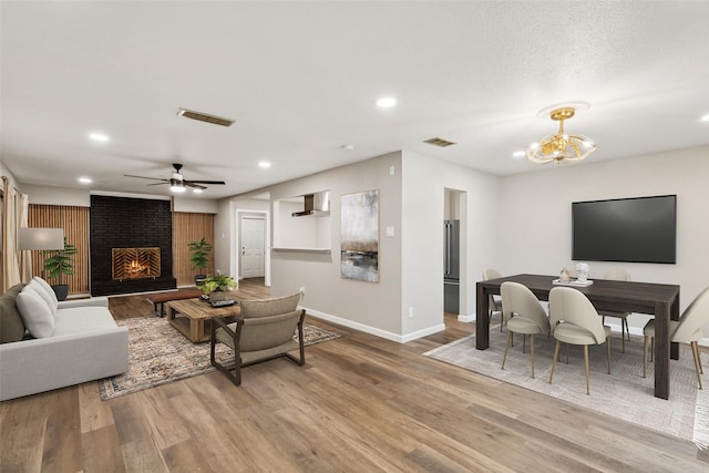 living room featuring wood-type flooring, ceiling fan with notable chandelier, and a brick fireplace