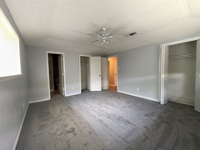 unfurnished bedroom with ceiling fan, dark carpet, a textured ceiling, and multiple closets