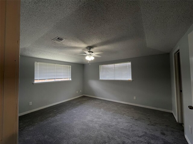 empty room featuring ceiling fan, dark carpet, and a textured ceiling