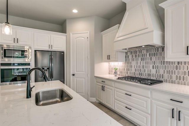 kitchen with premium range hood, a sink, white cabinets, appliances with stainless steel finishes, and decorative light fixtures