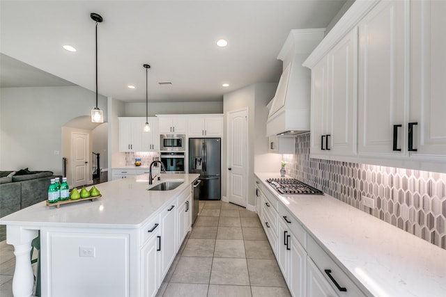 kitchen featuring stainless steel appliances, open floor plan, white cabinets, an island with sink, and premium range hood