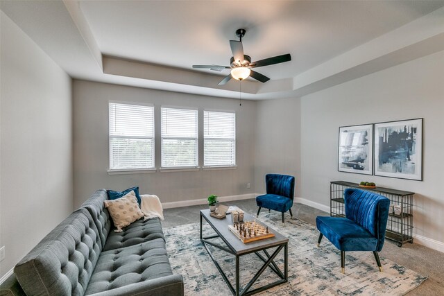 living room featuring a tray ceiling, carpet, a ceiling fan, and baseboards