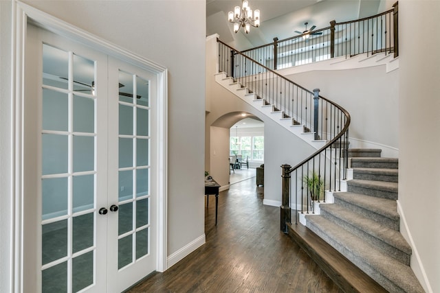 foyer entrance with ceiling fan with notable chandelier, a towering ceiling, dark wood-type flooring, and french doors