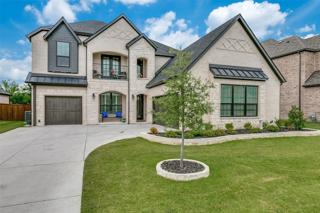 french country style house with a balcony, a standing seam roof, a front lawn, and concrete driveway