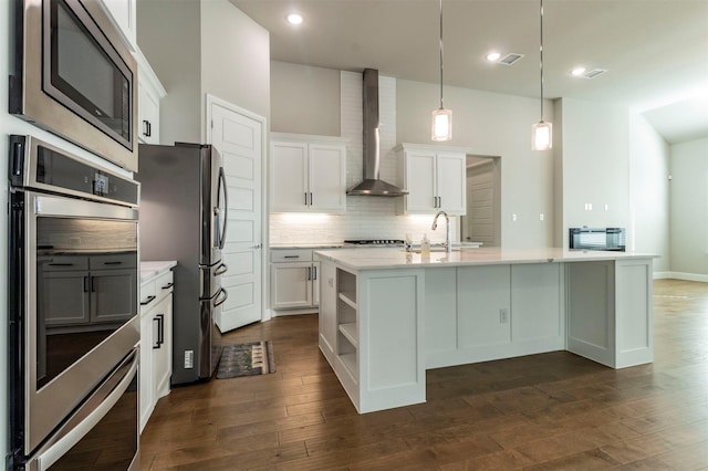 kitchen with an island with sink, pendant lighting, wall chimney range hood, and white cabinets