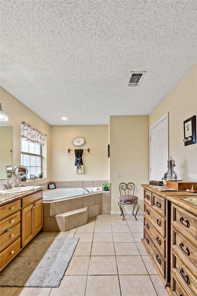 bathroom with vanity, a textured ceiling, tile patterned floors, and tiled tub