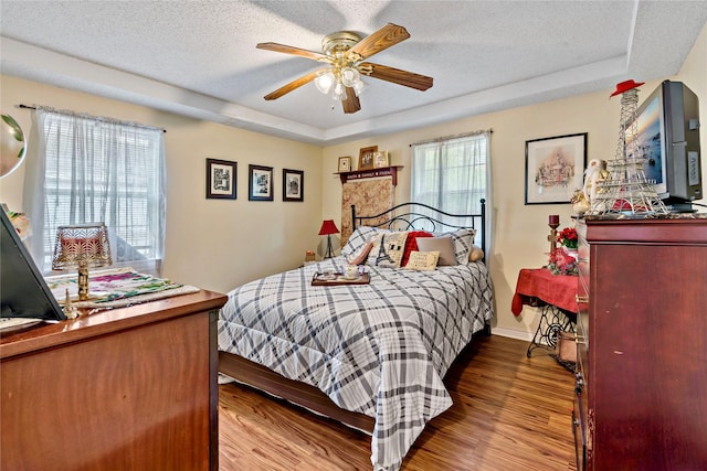 bedroom with ceiling fan, wood-type flooring, a textured ceiling, and a tray ceiling