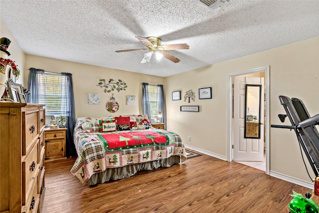 bedroom with ceiling fan, light hardwood / wood-style floors, a textured ceiling, and multiple windows