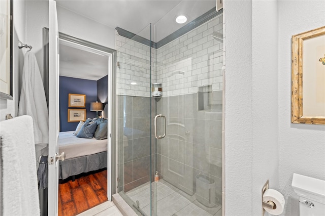 bathroom with wood-type flooring, toilet, and a shower with shower door