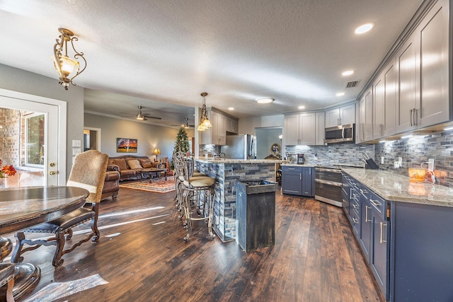 kitchen featuring a textured ceiling, stainless steel appliances, hanging light fixtures, and dark wood-type flooring