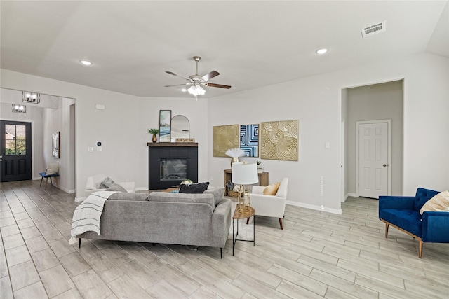 living room with ceiling fan with notable chandelier, light hardwood / wood-style floors, and a tiled fireplace