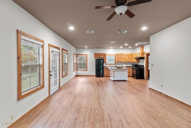 kitchen with light hardwood / wood-style flooring, electric range, a kitchen island, a kitchen bar, and black fridge