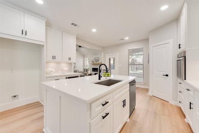 kitchen featuring stainless steel appliances, a sink, light wood-style flooring, and an island with sink