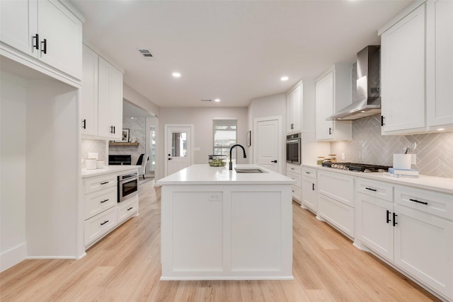 kitchen featuring stainless steel appliances, a sink, visible vents, wall chimney range hood, and light wood-type flooring