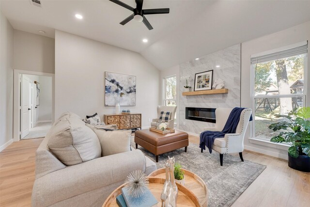 living room featuring lofted ceiling, light hardwood / wood-style flooring, a healthy amount of sunlight, and a premium fireplace