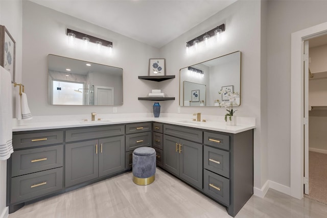 bathroom featuring double vanity, baseboards, walk in shower, and a sink