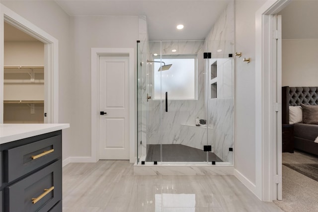 bathroom with a marble finish shower, a spacious closet, vanity, wood finished floors, and baseboards