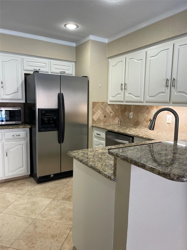 kitchen featuring white cabinetry, stainless steel appliances, tasteful backsplash, dark stone countertops, and ornamental molding