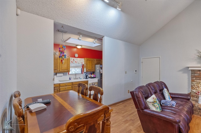 dining area featuring track lighting, sink, vaulted ceiling, light wood-type flooring, and a textured ceiling