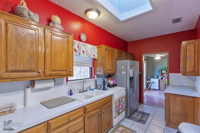 kitchen featuring dishwasher, sink, stainless steel fridge, a textured ceiling, and light tile patterned floors