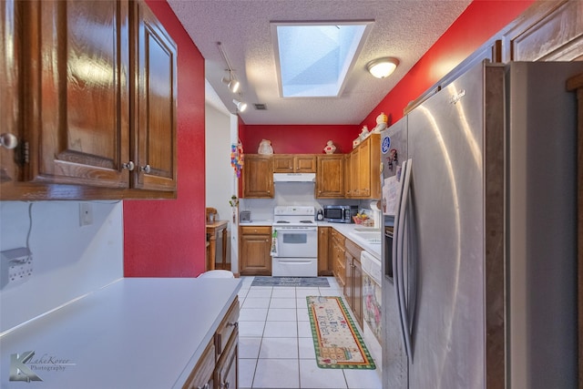 kitchen with a skylight, rail lighting, stainless steel appliances, a textured ceiling, and light tile patterned flooring