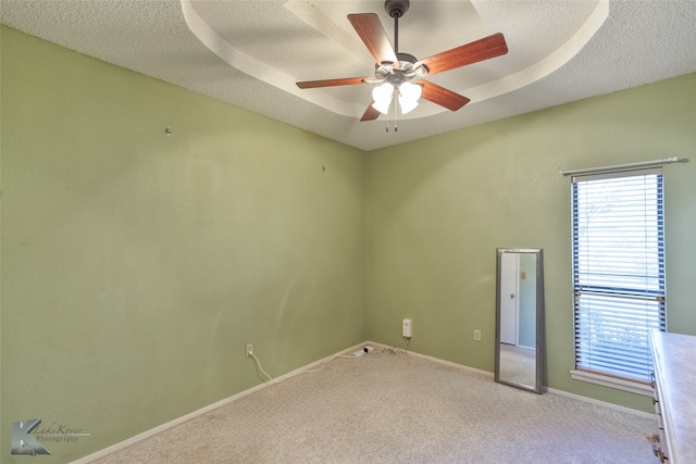 spare room with a tray ceiling, light carpet, ceiling fan, and a textured ceiling