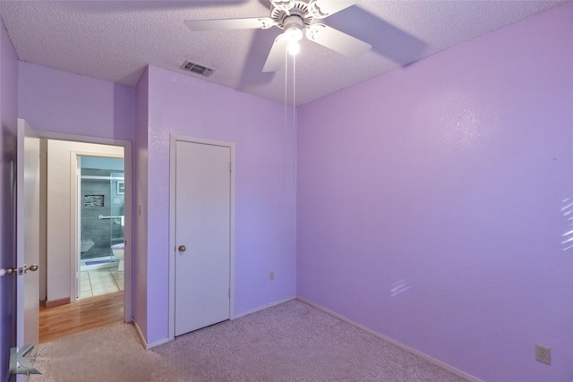 unfurnished bedroom featuring ceiling fan, a closet, light carpet, and a textured ceiling