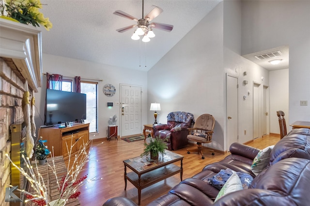 living room featuring a textured ceiling, light hardwood / wood-style floors, high vaulted ceiling, and ceiling fan