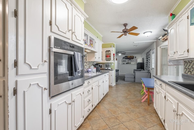 kitchen with decorative backsplash, stainless steel oven, white cabinetry, and a textured ceiling