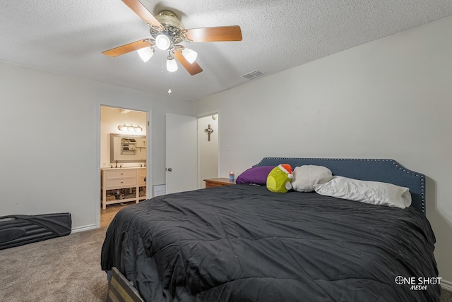 bedroom with ceiling fan, carpet, ensuite bathroom, and a textured ceiling