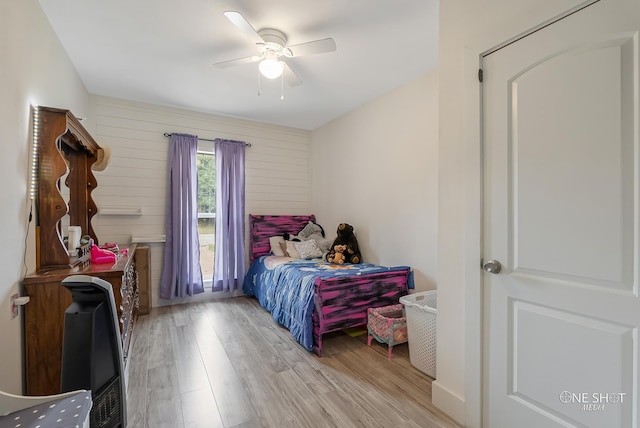 bedroom with ceiling fan, light hardwood / wood-style floors, and wooden walls